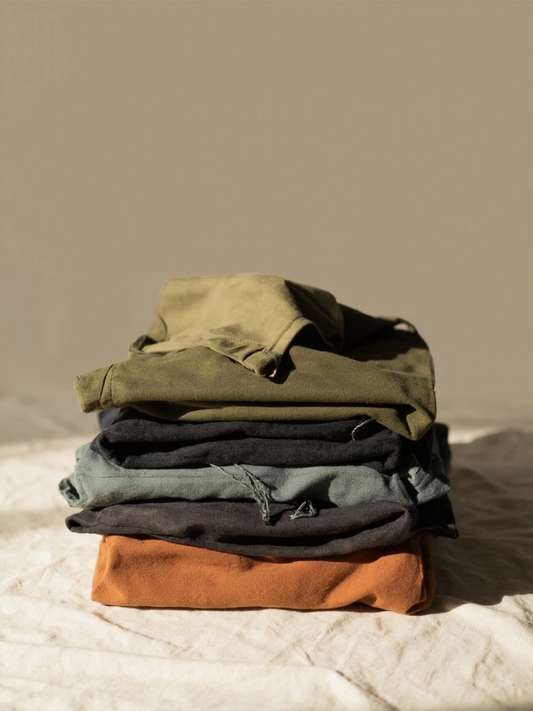 A folded stack of ShyRanger earth-tone apparel on a neutral linen surface.